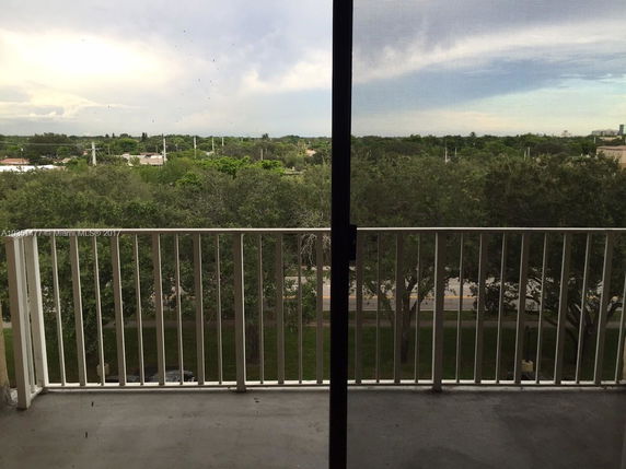 View from a balcony overlooking a landscape with trees and distant buildings.