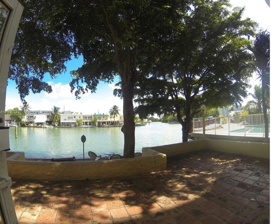View of a waterfront area with trees, a pool, and buildings across the water.