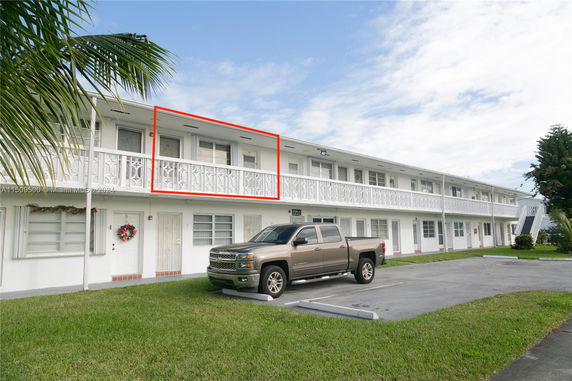Front view of a two-story apartment building with a balcony and a parked truck.