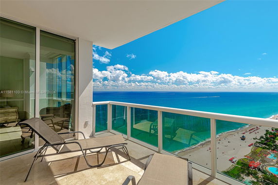 Balcony view overlooking a beach and ocean with lounge chairs.