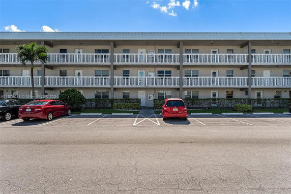 Front view of a multi-story building with balconies and parking spaces.