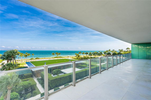 Panoramic view from a balcony overlooking the ocean with clear skies and palm trees.
