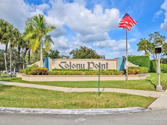 View of a sign for Colony Point surrounded by palm trees and greenery.