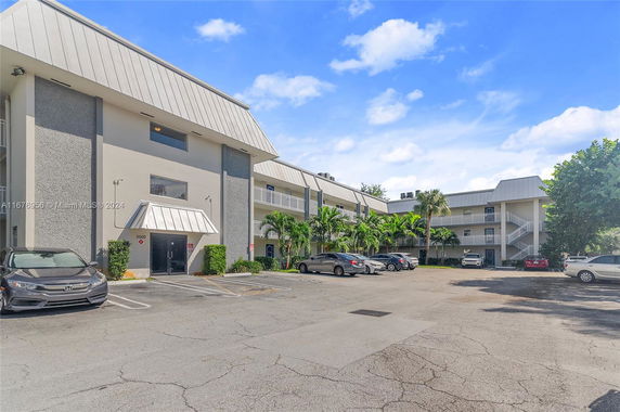 Parking area in front of a multi-story building with balconies and angled roof.