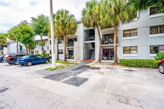 Outdoor parking area in front of a multi-story residential building with palm trees.