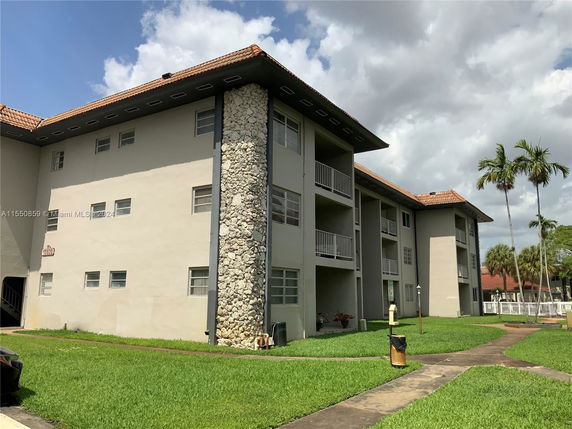 Front view of a multi-story apartment building with balconies and a stone accent wall.