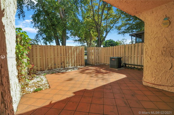 Outdoor tiled patio area with a wooden fence and some plants.