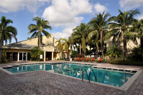 Outdoor swimming pool area with surrounding palm trees and a nearby building.