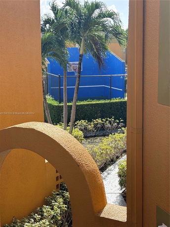 View of a basketball court with a blue wall and palm trees.