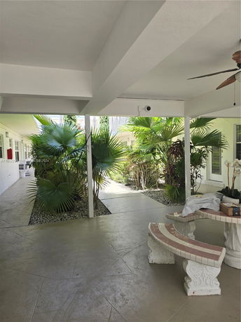 Covered outdoor area with bench near a building, surrounded by plants.
