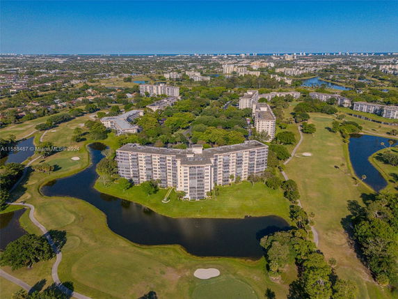 Aerial view of a large residential building surrounded by green lawns and ponds, with other buildings in the distance.
