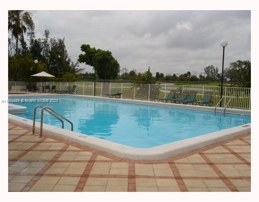 Outdoor swimming pool with lounge chairs and umbrella nearby.