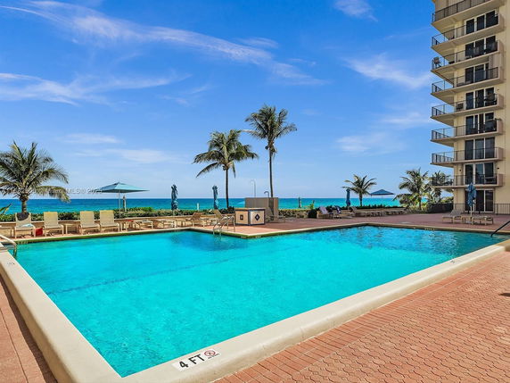 Outdoor swimming pool area with ocean view and lounge chairs.