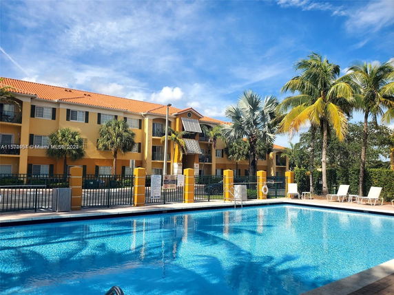 Outdoor pool area in front of a three-story building with orange roof and palm trees.