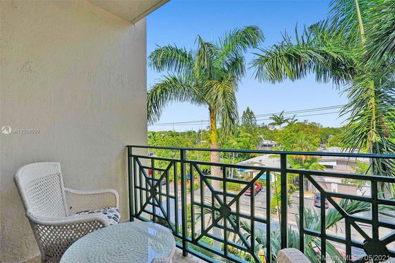 View from a balcony with green railing, overlooking palm trees and residential area.
