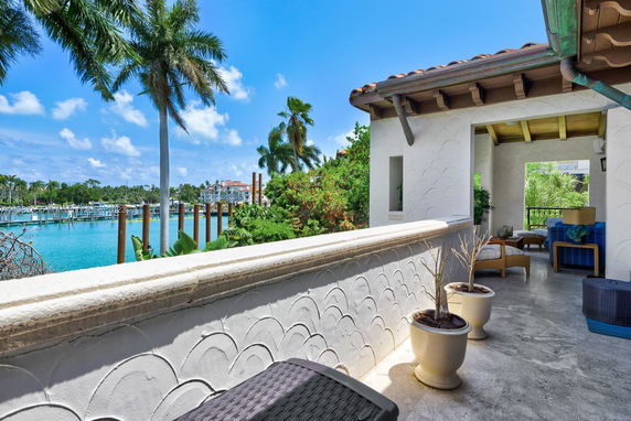 Outdoor terrace with decorative wall tiles and potted plants, overlooking a body of water with palm trees.