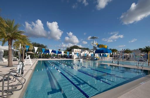 Outdoor swimming pool with lanes, surrounded by palm trees, and a slide area with water features.