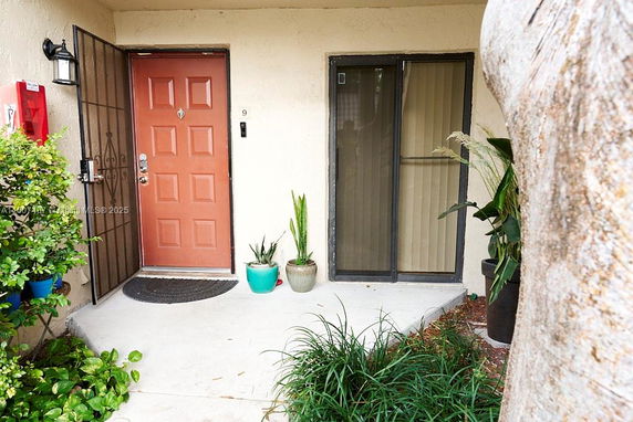 Front view of an entrance with a red door and a glass sliding door beside it, flanked by potted plants.