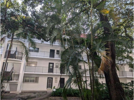 Front view of a multi-story building with balconies surrounded by trees.