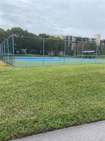 Tennis court surrounded by a fence with a building in the background.