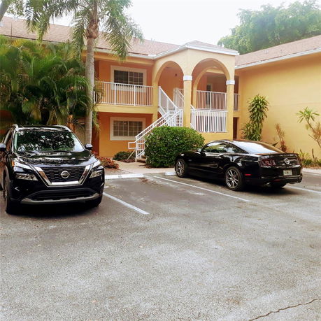 Outdoor parking area in front of a two-story building with arches and white railings.