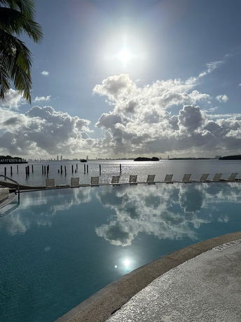 Swimming pool with lounge chairs overlooking a body of water and city skyline.