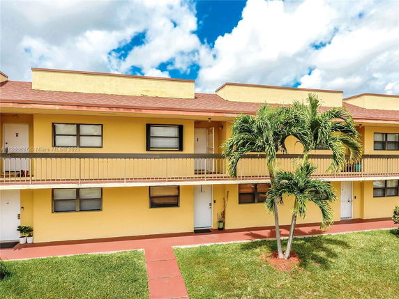 Front view of a two-story residential building with balconies and yellow exterior walls.