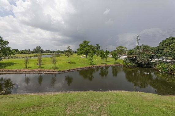 View of a lush landscape with a pond, grass, and trees under a cloudy sky.