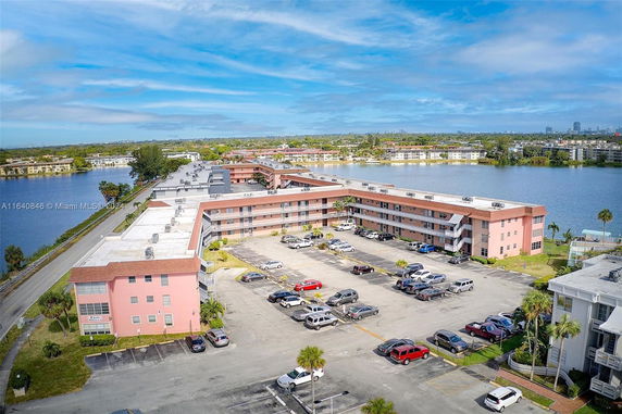 Aerial view of a multi-story residential complex near a body of water with parking area.