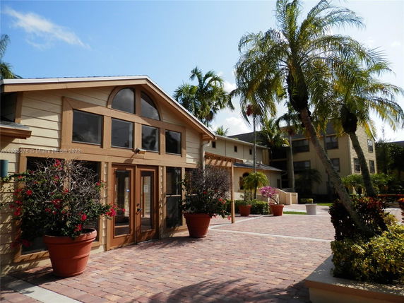Front view of a single-story building with large windows and potted plants, surrounded by palm trees.