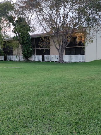Front view of a two-story building with large trees and a grassy lawn.