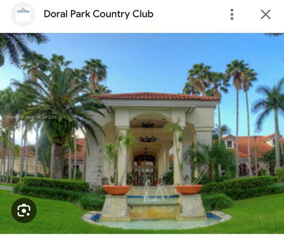 Front view of a country club building with palm trees and an entrance fountain.