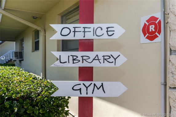 View of building exterior with directional signs for office, library, and gym.