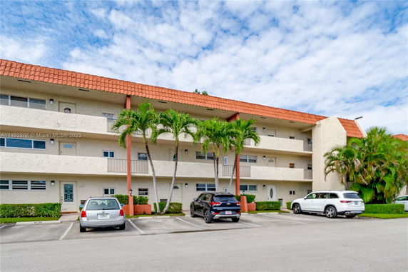 Front view of a multi-story apartment building with balconies and a parking area.