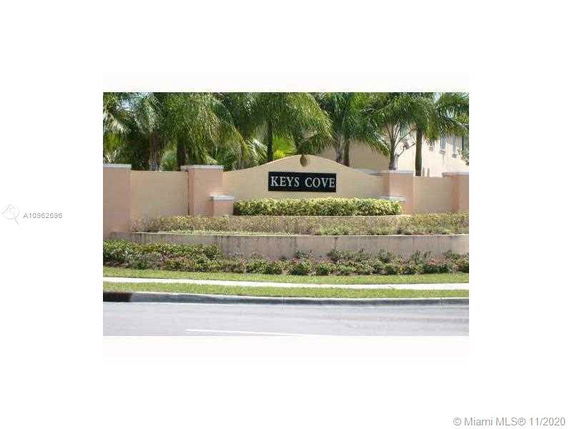 Entrance sign for Keys Cove with surrounding greenery and palm trees.