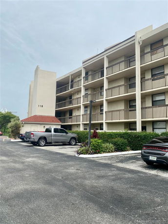 Front view of a multi-story building with balconies and a parking area.