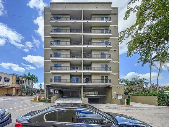 Front view of a multi-story residential building with balconies and an open parking area on the ground floor.