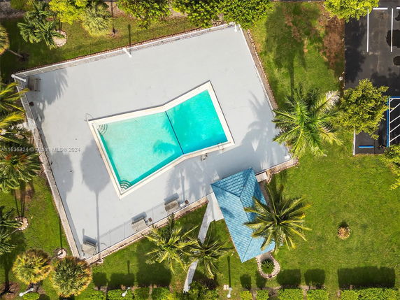 Aerial view of a unique-shaped swimming pool within a fenced area surrounded by greenery.
