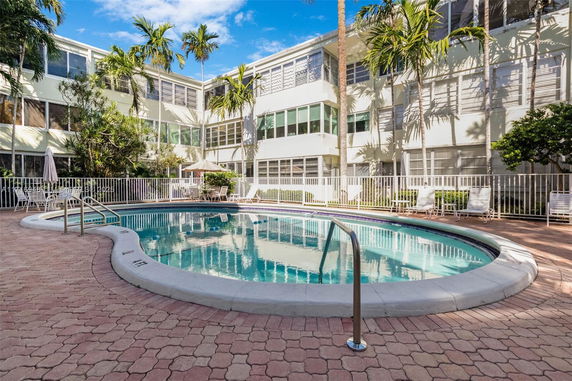 Outdoor swimming pool area with surrounding building and palm trees.