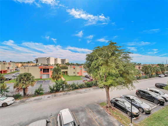 View of residential buildings and a parking area with trees under a blue sky.