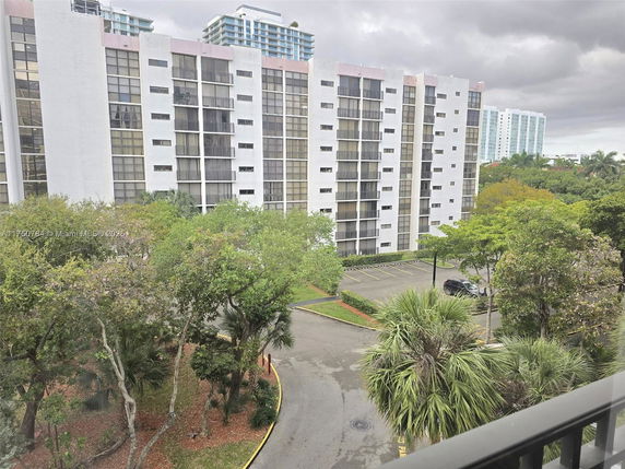 View of tall apartment buildings from a higher level, with parking area and trees in the foreground.