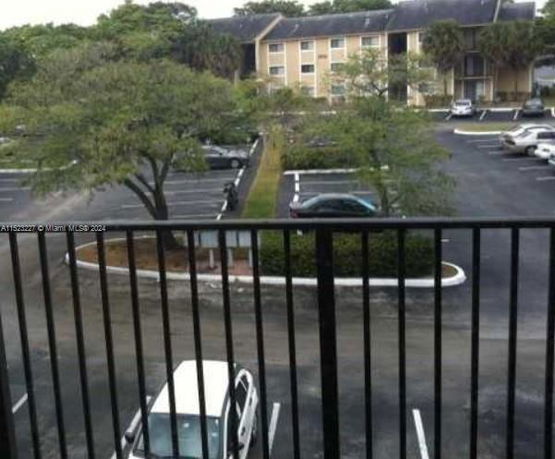 View from a balcony overlooking a parking area with several parked cars and buildings in the background.