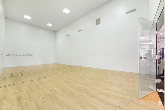 Interior view of a racquetball court with wooden flooring and glass door.