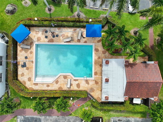 Aerial view of an outdoor swimming pool with surrounding patio and greenery.