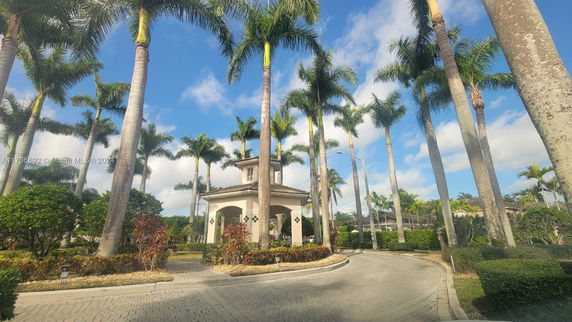 View of a small building surrounded by tall palm trees with a paved circular driveway.