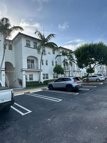 Front view of a multi-story residential building with arched balconies and parking area.