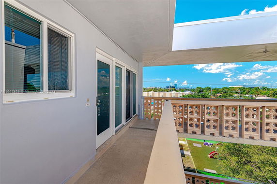 A balcony with decorative railing and glass doors, overlooking green lawns and cityscape in the distance.