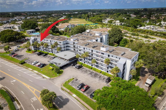 Aerial view of a multi-story building with a parking area, surrounded by greenery and other residential buildings.