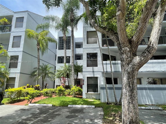 Front view of a multi-story residential building with balconies and surrounding greenery.
