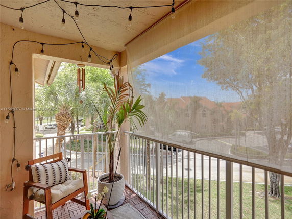 View from a balcony with outdoor seating overlooking a parking area and palm trees.